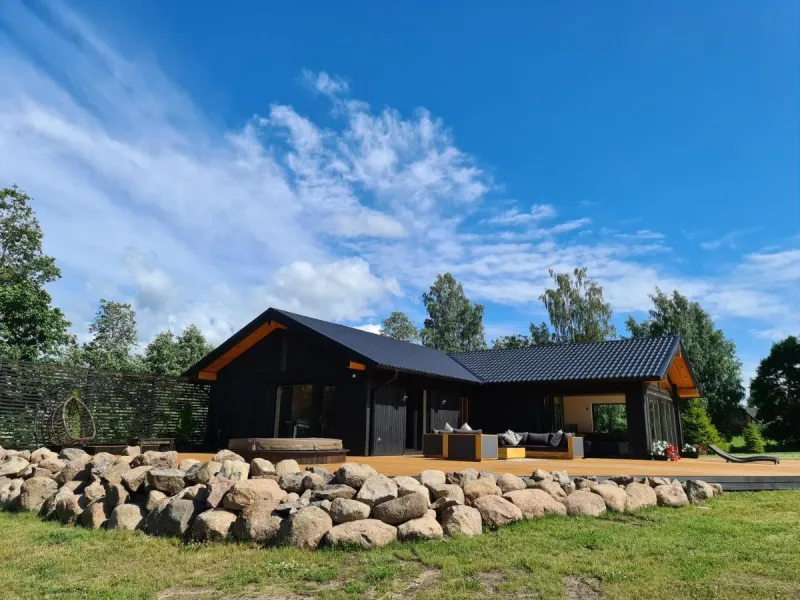 Svartmålat trähus med stor altan och stenmur